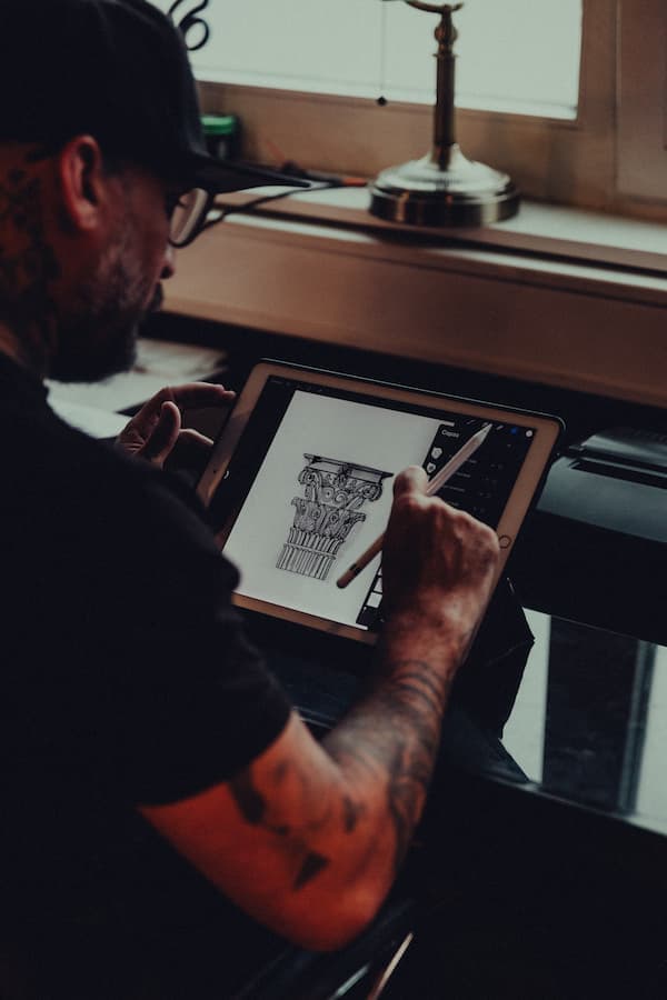 A tattooed artist sketching a design on paper at a wooden desk