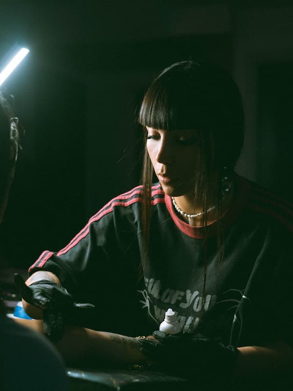 A tattoo artist working on a client's forearm in a sunlit studio